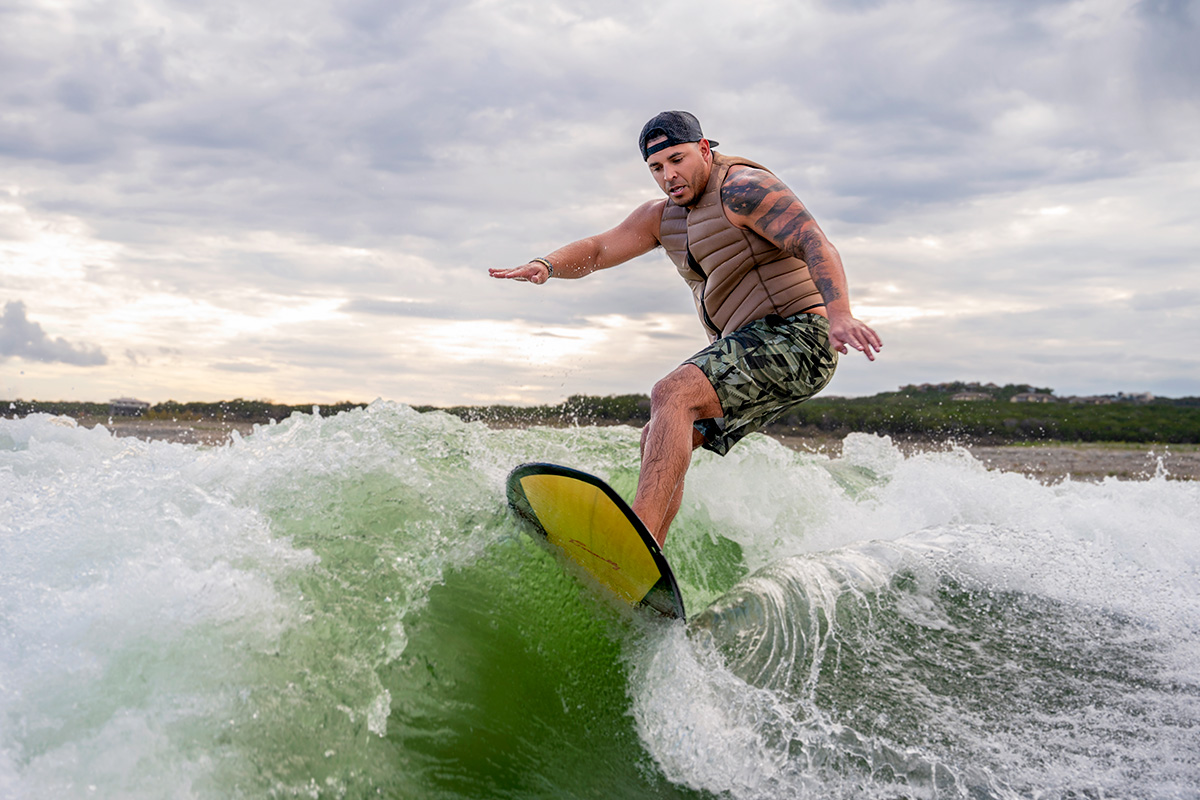Man with tan life vest and camo shorts in the ocean riding a yellow wakeboard