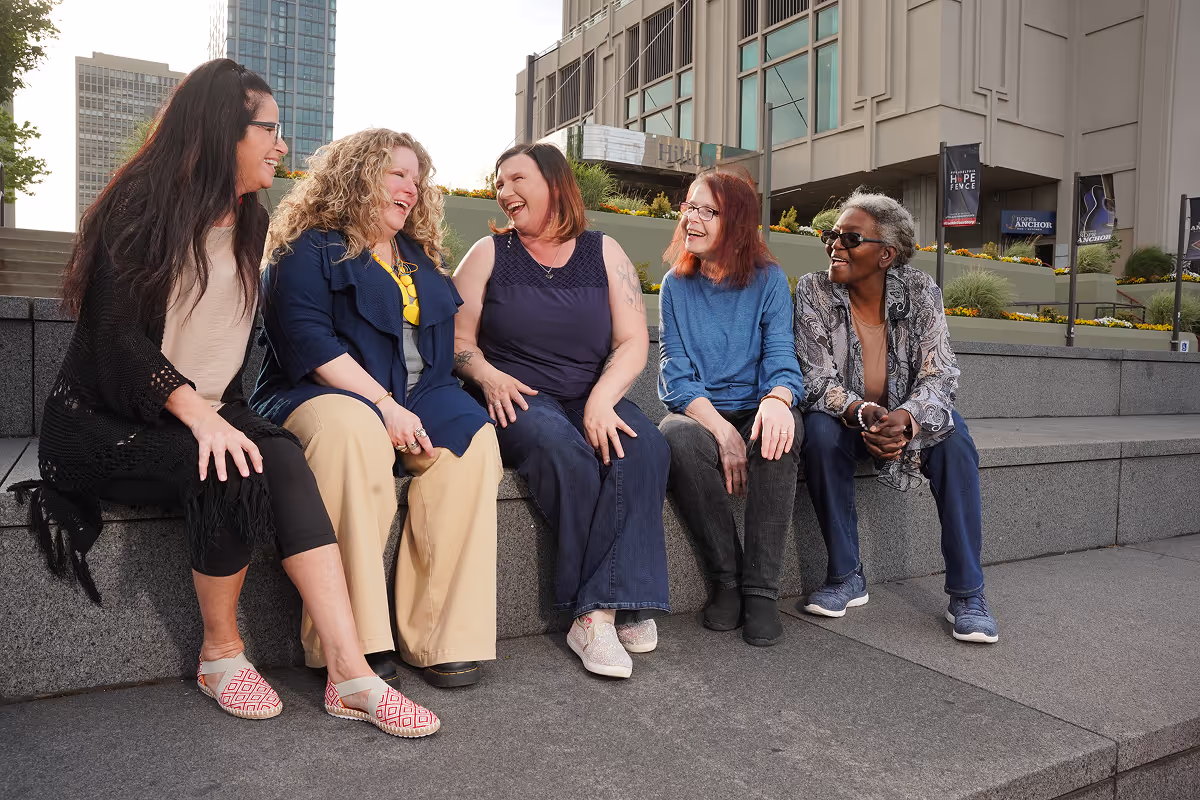 group of female friends sitting on a concrete bench in an urban setting smiling and laughing