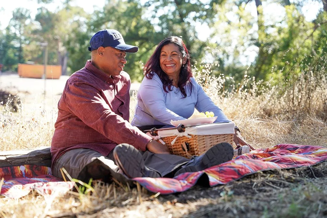 middle aged couple sitting on a blanket in the outdoors having a picnic