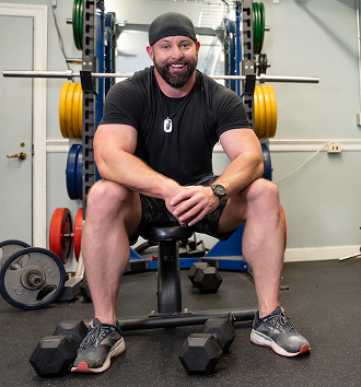 male Veteran in black shirt and shorts sitting on a bench   
press at the gym 