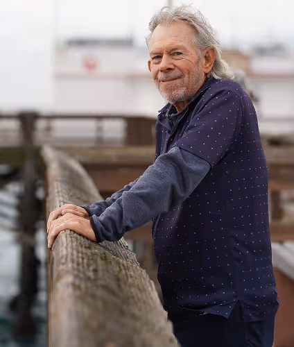 man in navy shirt smiling with hands on a balcony in an outdoor setting   